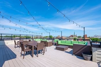 A rooftop patio with wooden flooring, tables and chairs, and string lights.